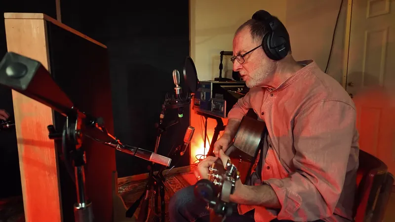 Seated with a guitar under red studio light